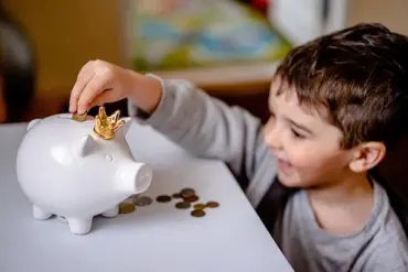 Foto, Kind wirft Geld in ein Sparschwein