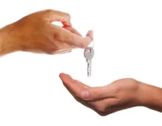 zwei Hände. Eine Hand übergibt einen Hausschlüssel der anderen Hand