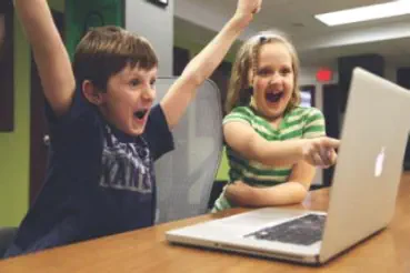 2 Kinder sitzen schreiend an einem Tisch und spielen am Computer