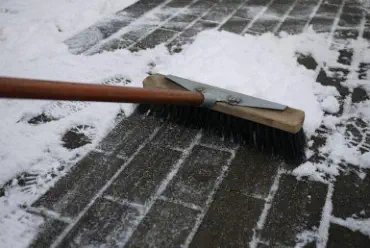 Ein Besen der Schnee von einem Gehweg wegfegt