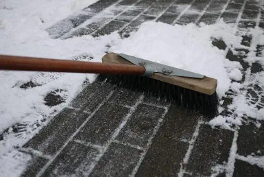 Ein Besen der Schnee von einem Gehweg wegfegt