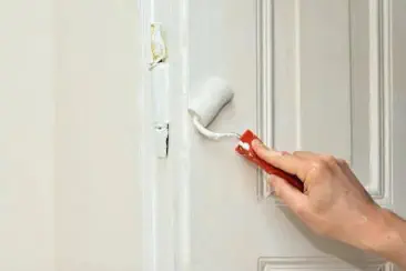 Eine Wohnungstür mit weißer Farbe überstrichen. Zu sehen ist nur eine Hand mit dem Farbroller.