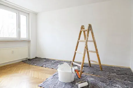 Heller Wohnraum bei Schönheitsreparaturen mit Leiter, Farbrolle und Abdeckfolie – Wohnung wird frisch gestrichen und renoviert 