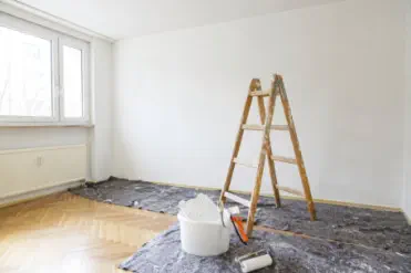 Heller Wohnraum bei Schönheitsreparaturen mit Leiter, Farbrolle und Abdeckfolie – Wohnung wird frisch gestrichen und renoviert 
